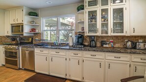 A kitchen with white cabinets, a granite countertop, stainless steel appliances, and a large window.