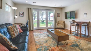 A living room with a leather couch, a coffee table, a TV, and a dining area with chairs and a bar stool.