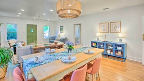 A dining area with a wooden table set for four, surrounded by pink chairs, a blue cabinet with shelves, and a hanging wicker chandelier. - Newly Updated & Charming Azalea District Home (Tyler)
