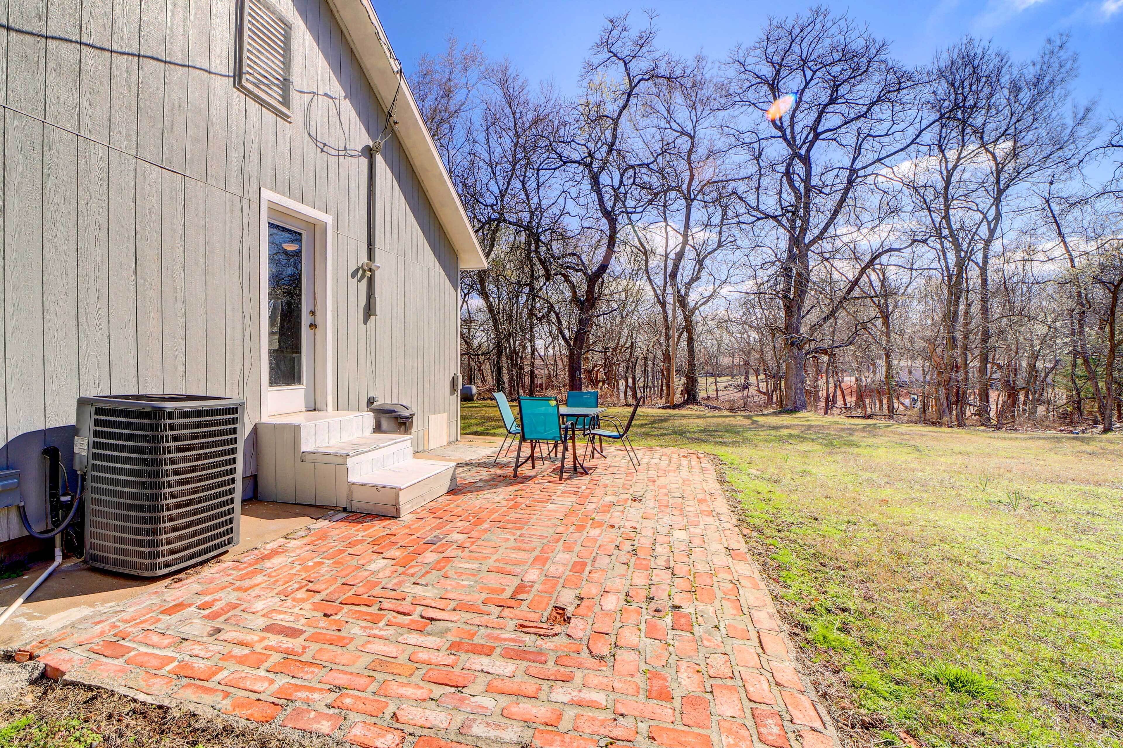 A brick patio with outdoor furniture, a large air conditioning unit, and a house with a wooden exterior.