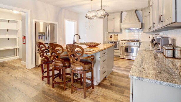 A modern kitchen with a central island, wooden chairs, and built-in appliances. - Game Room + Large Backyard: Afton Home! (Afton)