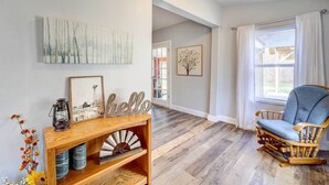 A room with a wooden floor, a rocking chair, a console table with a lantern, and wall art. - Game Room + Large Backyard: Afton Home! (Afton)