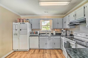 A kitchen with white cabinets, a refrigerator, a dishwasher, a stove, and a window.