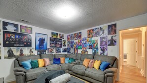 A living room with a sectional sofa, colorful pillows, and a wall adorned with various posters. - Pet-friendly Jacksonville Home w/ Fenced Yard (Jacksonville)