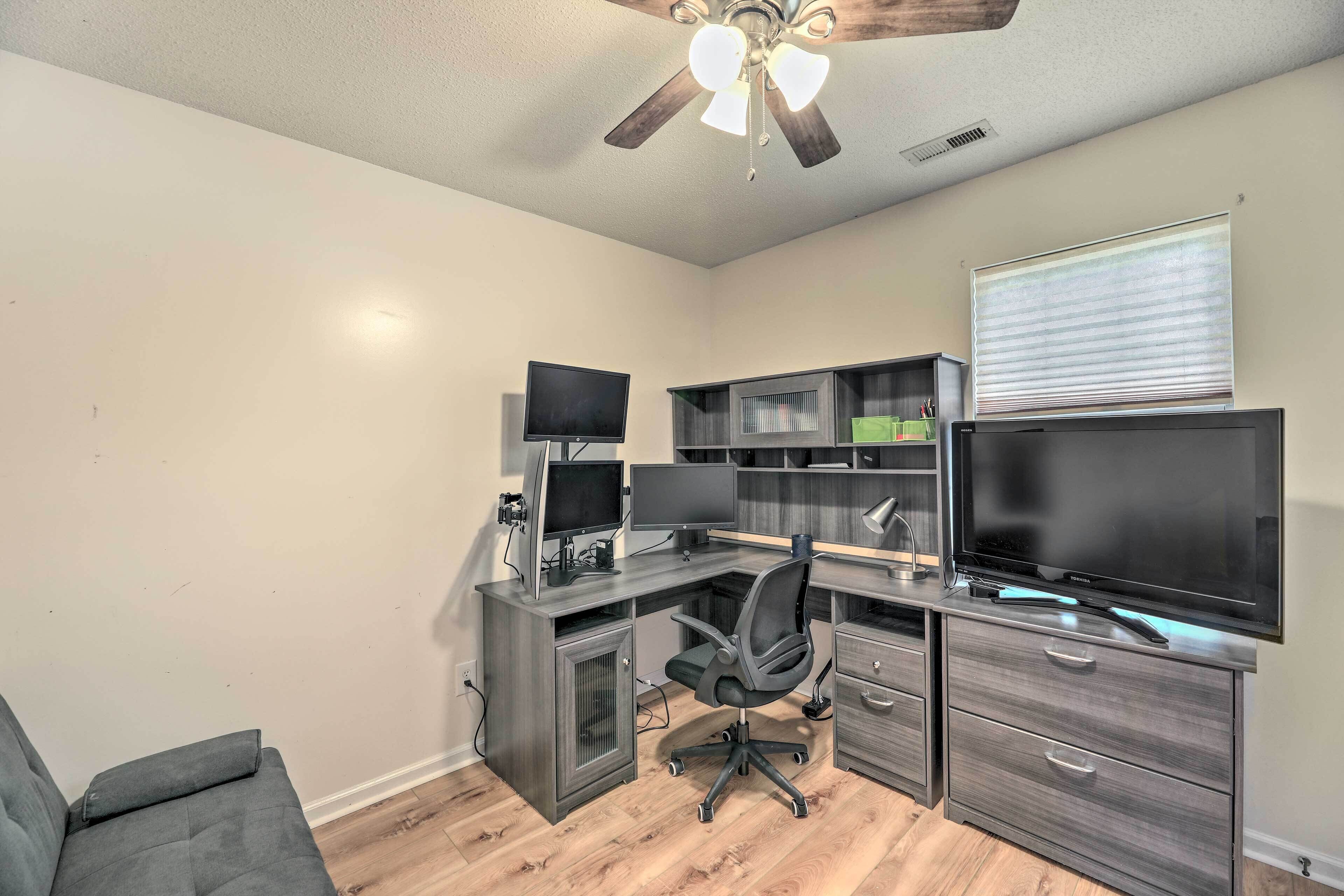 A home office with a desk, computer monitors, and a television.