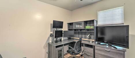 A home office with a desk, computer monitors, and a television.