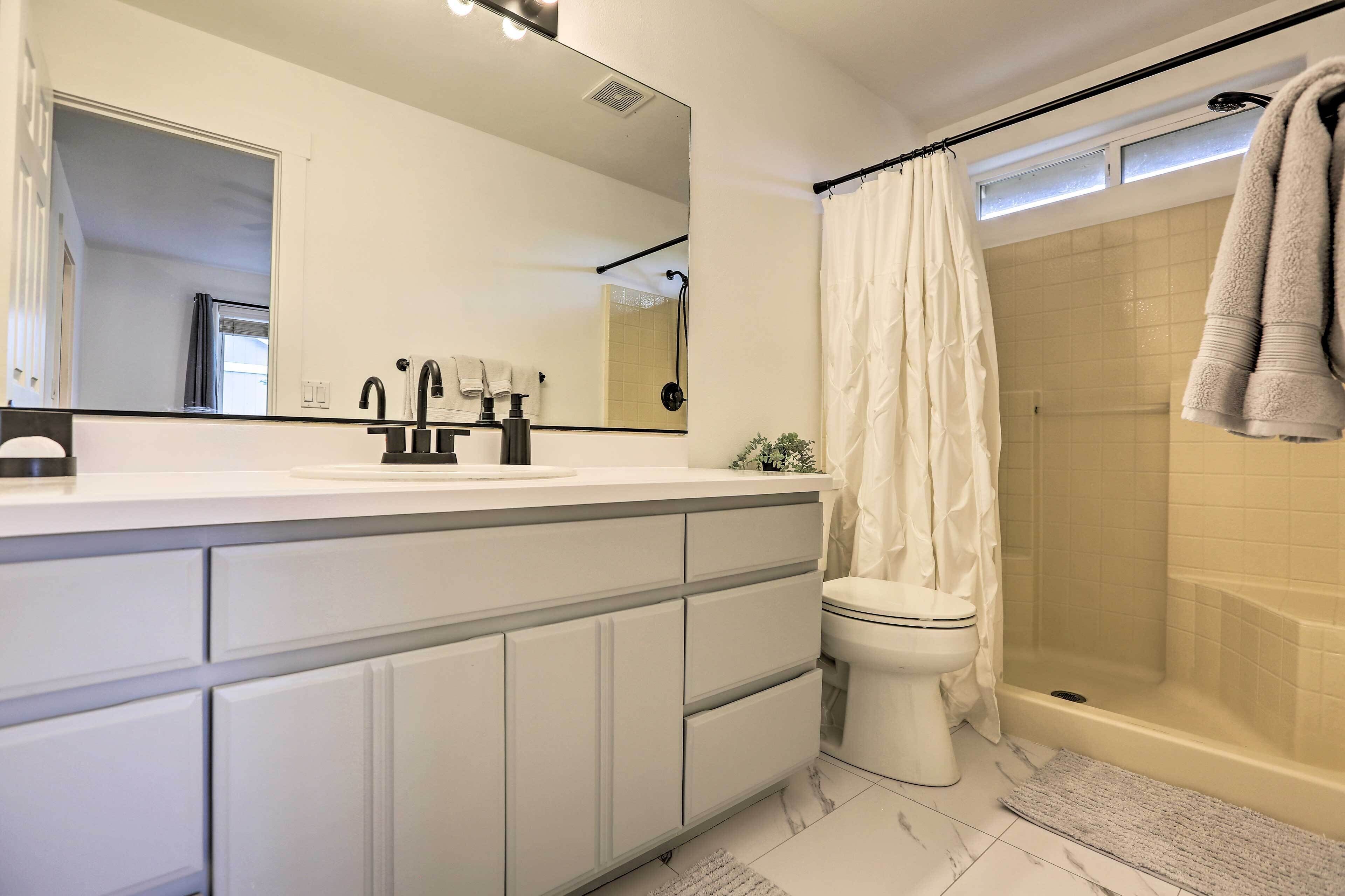 Une salle de bain moderne avec un meuble-lavabo blanc, un grand miroir, des toilettes et une douche à l’italienne.