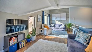 Uma sala de estar moderna com uma televisão de tela plana, um sofá, uma mesa de centro e uma área de jantar com mesa e cadeiras.