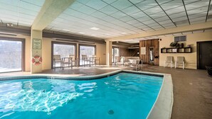 Piscina interna com teto azulejado, janelas e área de estar com cadeiras e mesas.