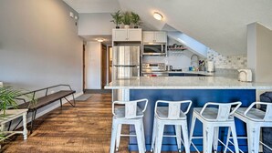 Cozinha moderna com ilha central, banquetas e escada para um andar superior.