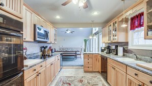 A kitchen with wooden cabinets, a microwave, an oven, and a dining area with a bench. - Resort Home on Mountain Golf Course w/ Deck & View (McGaheysville)