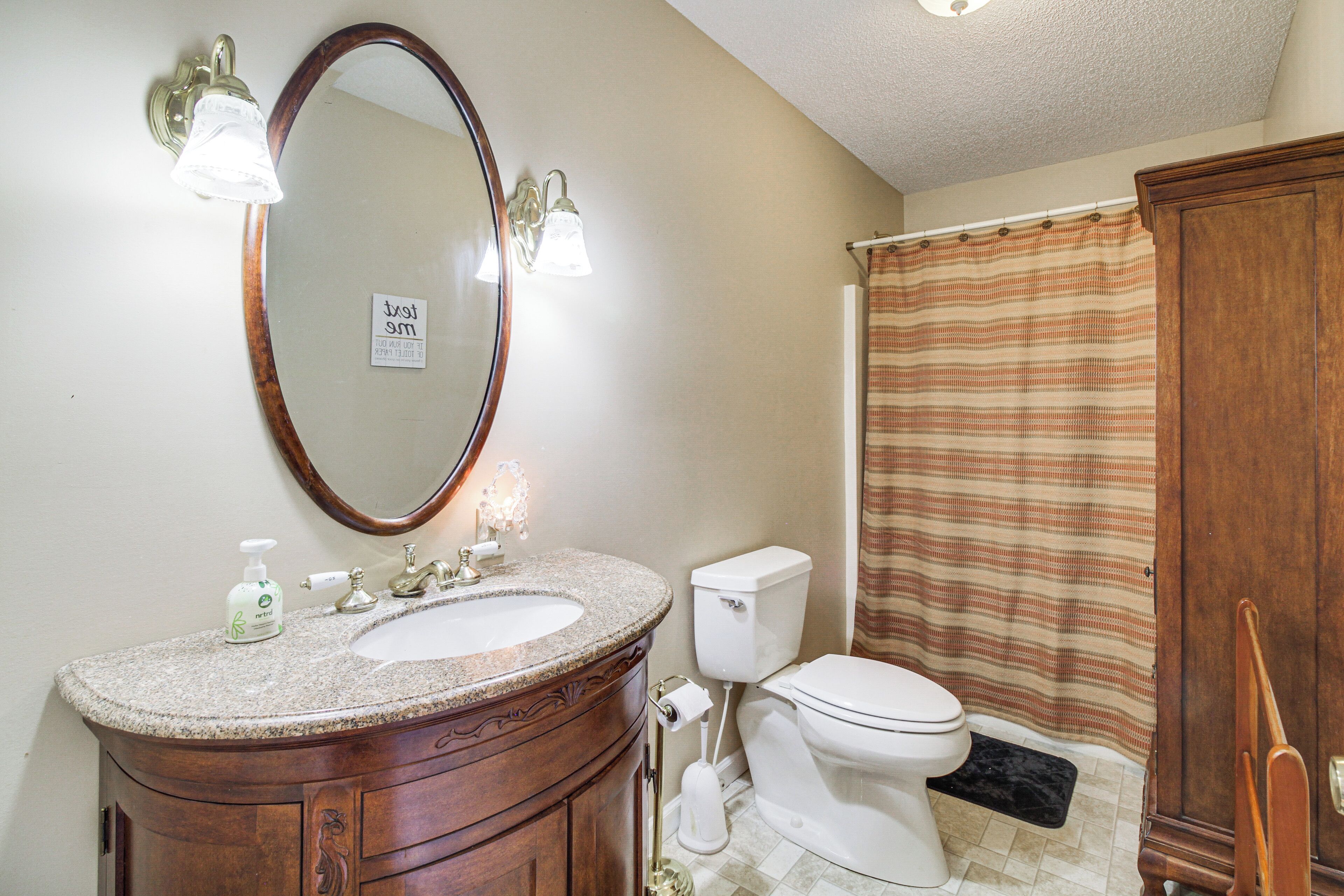 A bathroom with a wooden vanity, a sink, a mirror, a toilet, and a shower curtain.