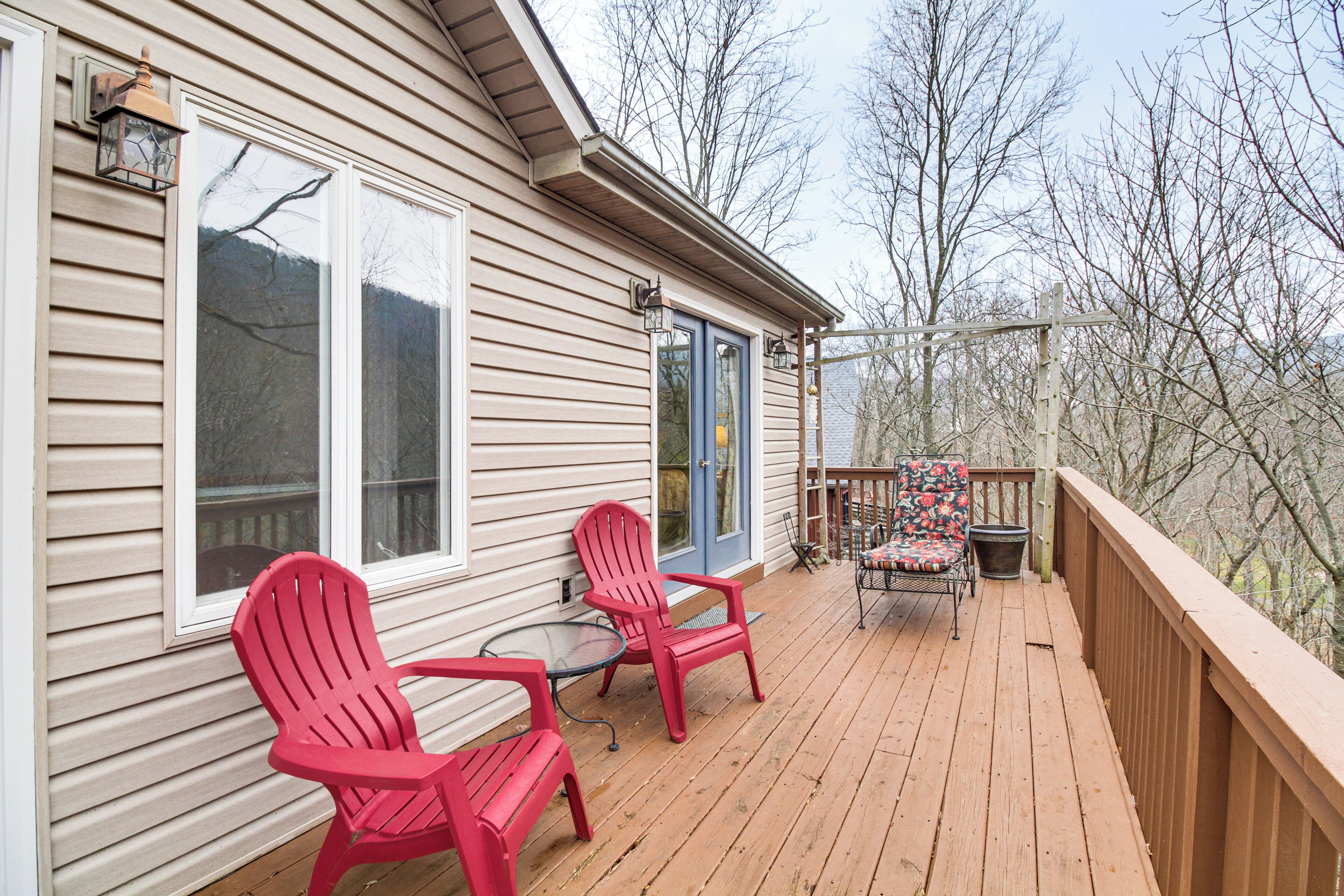 A wooden deck with two red Adirondack chairs and a small table, overlooking a forested area.