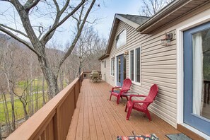A wooden deck with red chairs and a table, overlooking a landscape with trees and a distant view. - Resort Home on Mountain Golf Course w/ Deck & View (McGaheysville)