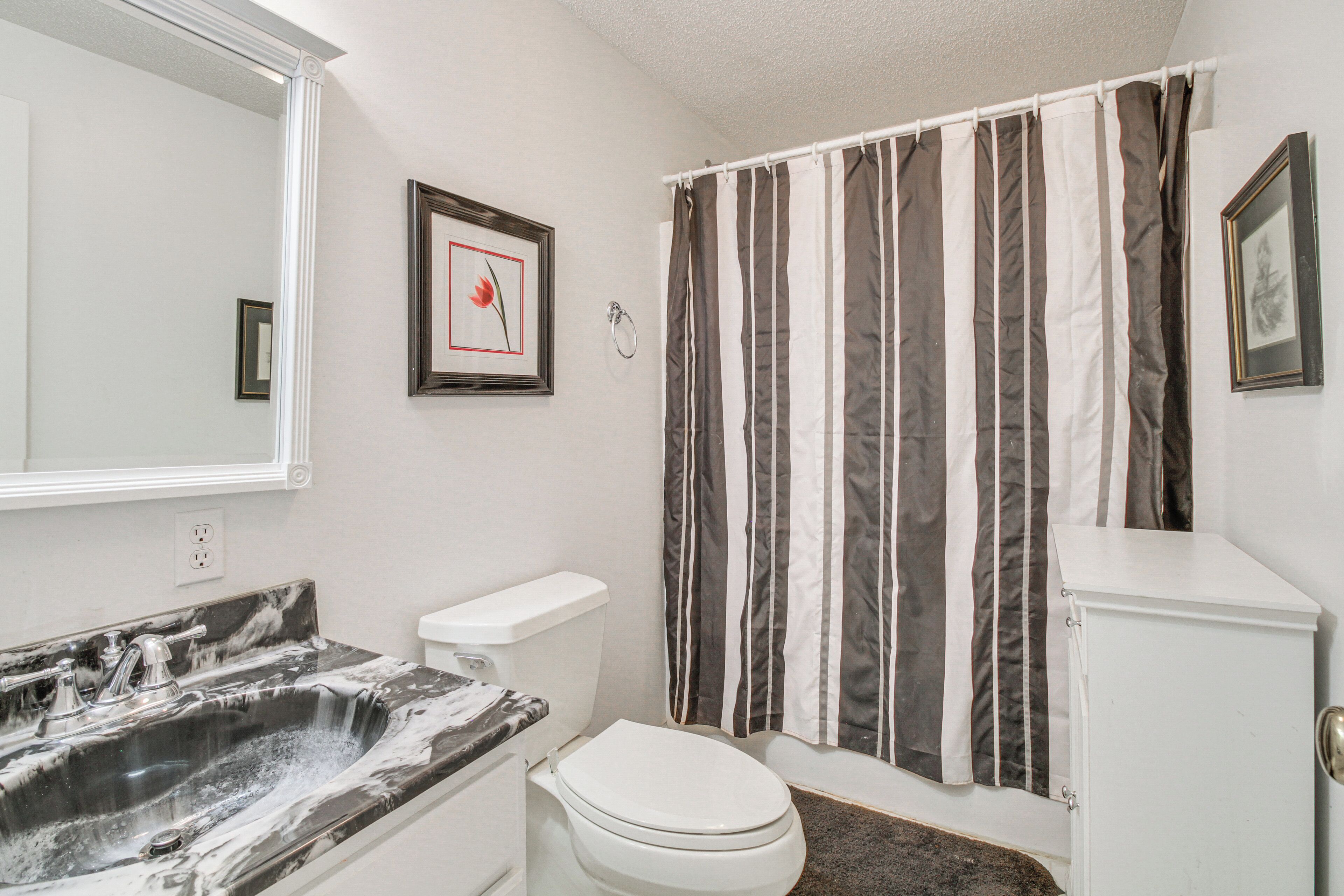 A bathroom with a marble sink, white toilet, striped shower curtain, and framed pictures on the wall.