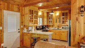 A wooden cabin interior with a kitchen, bar stools, a coffee maker, and a fireplace. - 3 Mi to Big Trees State Park: Cabin w/ Scenic Deck (Arnold)