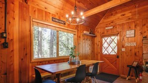 A wooden cabin interior with a dining table, chairs, a chandelier, a large window, and a door labeled "Snowboarding". - 3 Mi to Big Trees State Park: Cabin w/ Scenic Deck (Arnold)