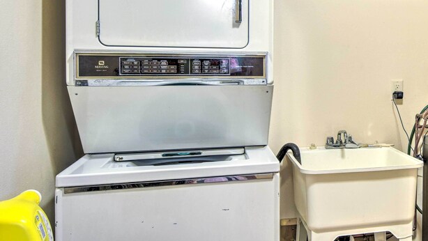 Eine weiße Maytag Waschmaschine und ein Trockner mit Bedienfeld, ein gelbes Reinigungsprodukt und ein weißes Waschbecken mit Wasserhahn.