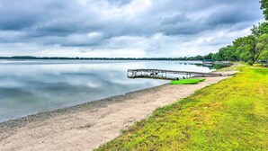 A calm lake with a dock, a green boat, and a grassy area. - Lakefront Spicer Cabin w/ Dock & 2 Kayaks! (Spicer)