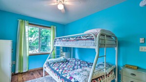 Ein Stockbett in einem Zimmer mit blauen Wänden, einem Fenster mit grünen Vorhängen, einem Deckenventilator und einer kleinen, weißen Kommode.