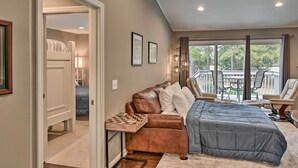 A bedroom with a large bed, a seating area with a table, and a view of the outdoors through a sliding glass door. - Pinehurst Gem on Golf Course & Putting Green! (Pinehurst)