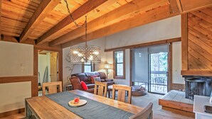 Una mesa de comedor de madera con sillas, un sofá y una chimenea en una habitación acogedora con vigas de madera y ventanas amplias.