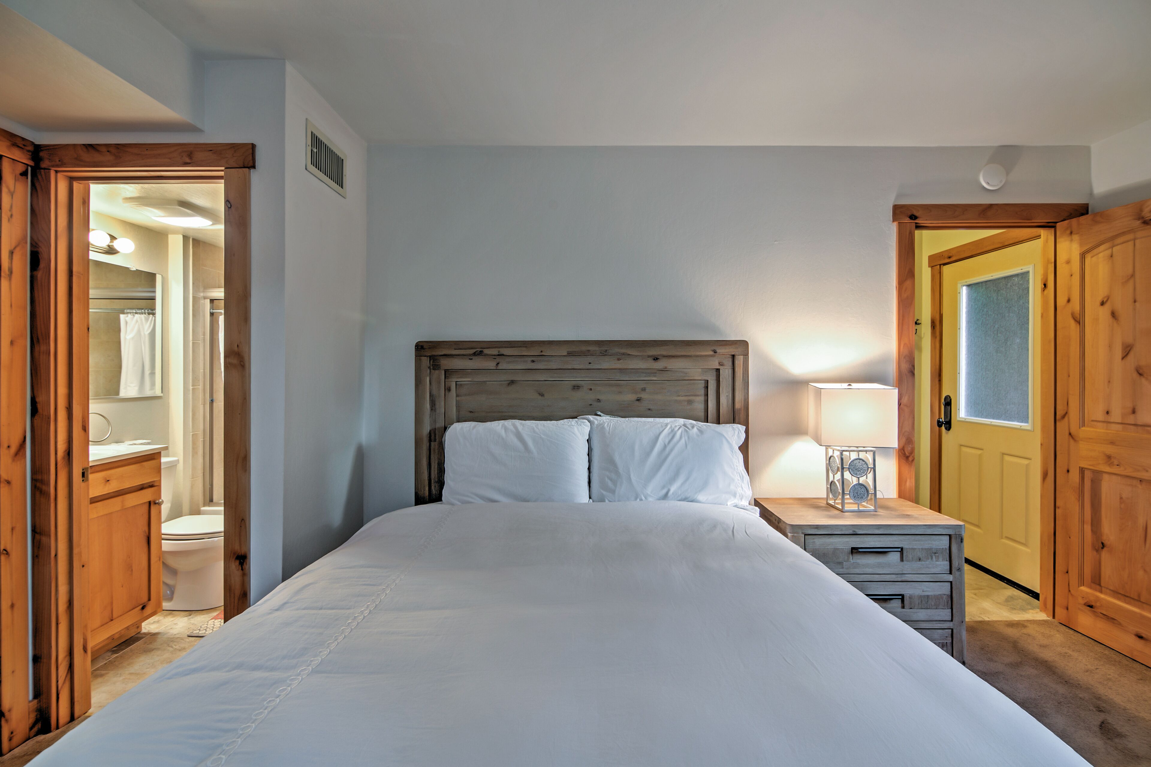 A bedroom with a wooden headboard, a bed with white bedding, a bedside table with a lamp, and a wooden wardrobe.