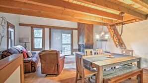 Amplia sala de estar con techo de madera, chimenea, mesa de comedor con sillas y sof á con cojines.