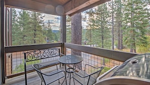 Un espacio al aire libre cubierto con mesa y sillas de metal, con vistas a una zona boscosa.