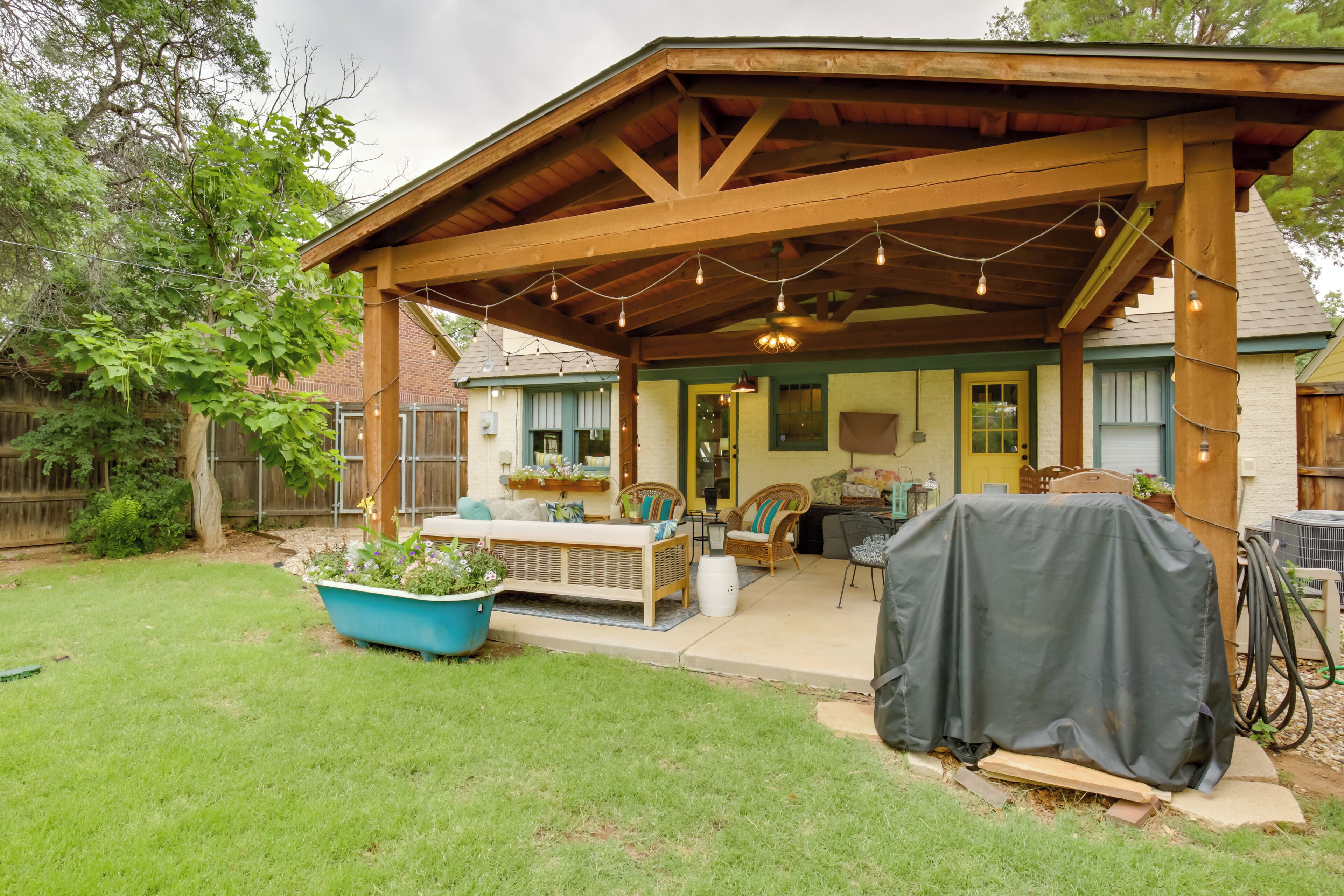 A covered patio with wooden beams, string lights, and outdoor furniture.