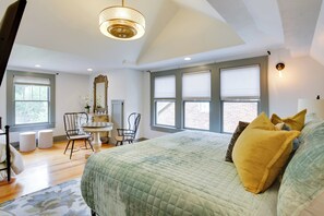 A bedroom with a large bed, a desk, two chairs, a mirror, and a window with blinds. - Renovated Lubbock Home - Walk to Texas Tech! (Lubbock)