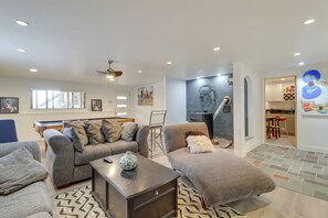 A modern living room with a sofa, armchair, and coffee table. There is a pool table and a painting on the wall.