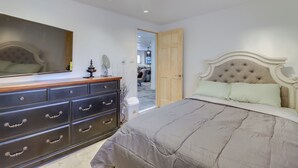 Een slaapkamer met een groot bed, een dressoir met meerdere lades, een spiegel en een deur naar een andere kamer.