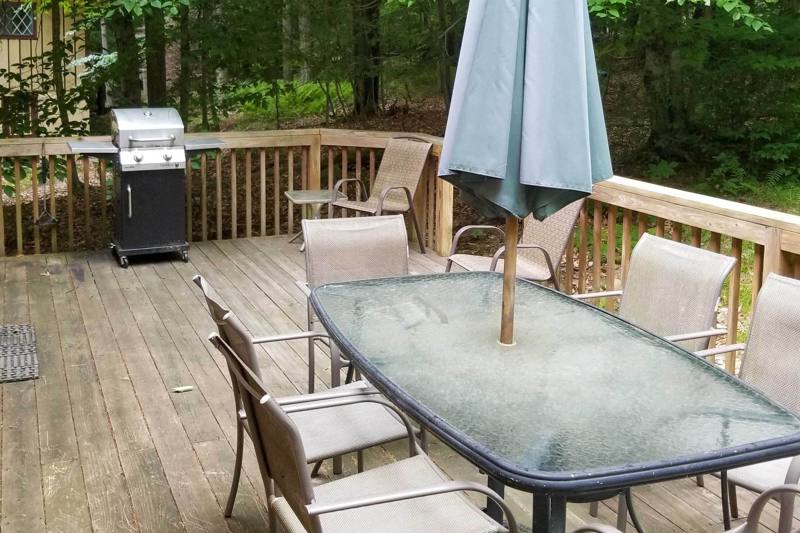 A wooden deck with a glass table and chairs, a grill, and an umbrella.