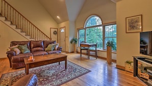 A spacious living room with a leather sofa, wooden coffee table, and a large window providing a view of the outdoors. - Pocono Mountain Home w/ 3 Community Lakes! (Gouldsboro)
