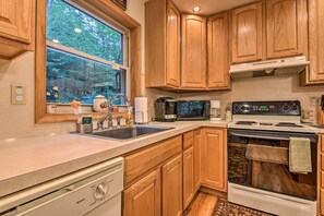 A kitchen with wooden cabinets, a stainless steel sink, a microwave, a stove, and a window with a view of trees. - Pocono Mountain Home w/ 3 Community Lakes! (Gouldsboro)