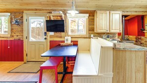 Une cuisine de taille réduite, avec des meubles de rangement en bois, un banc, un téléviseur et une porte rouge.
