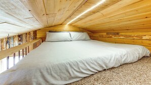 Une chambre confortable avec un plafond en bois, un lit recouvert de draps blancs et une vue par la fenêtre.