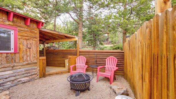 Une cabane en bois avec un foyer et deux fauteuils Adirondack roses.