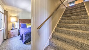 A bedroom with a bed, nightstand, lamp, and a staircase. - Relaxing Ruidoso Getaway w/ Spacious Deck! (Ruidoso)