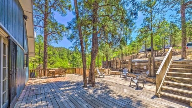 A wooden deck with outdoor seating, surrounded by tall pine trees. - Relaxing Ruidoso Getaway w/ Spacious Deck! (Ruidoso)
