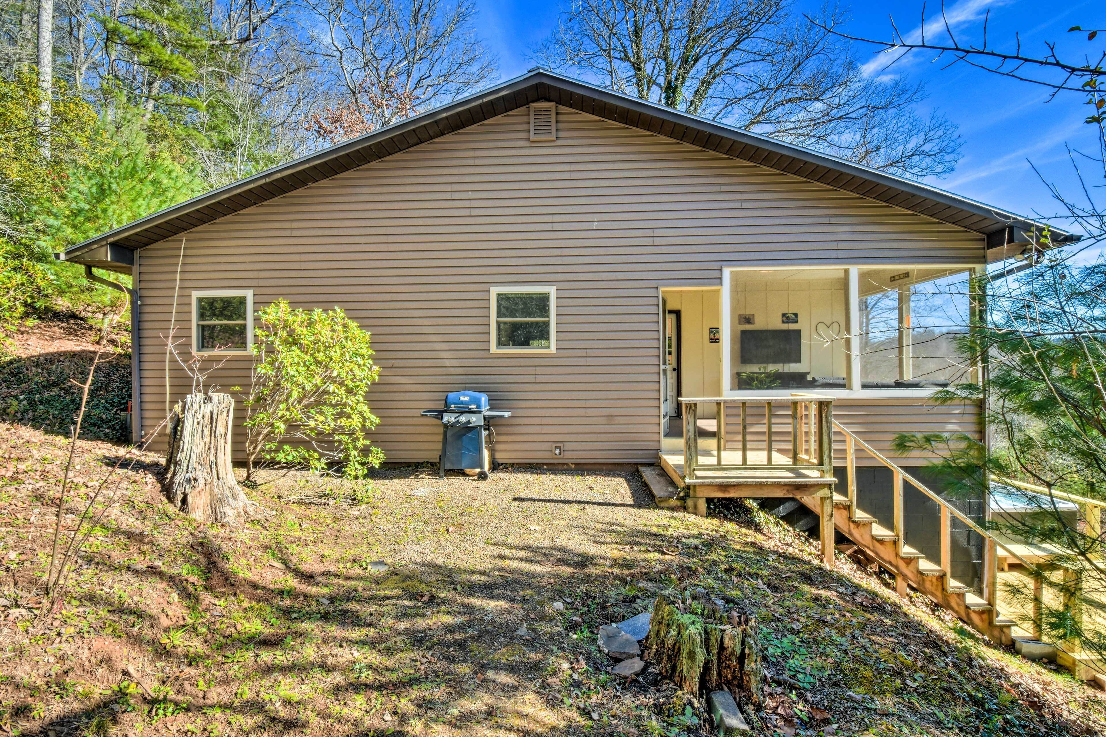 A single-story cabin with a covered porch, a small deck, and a grill outside.