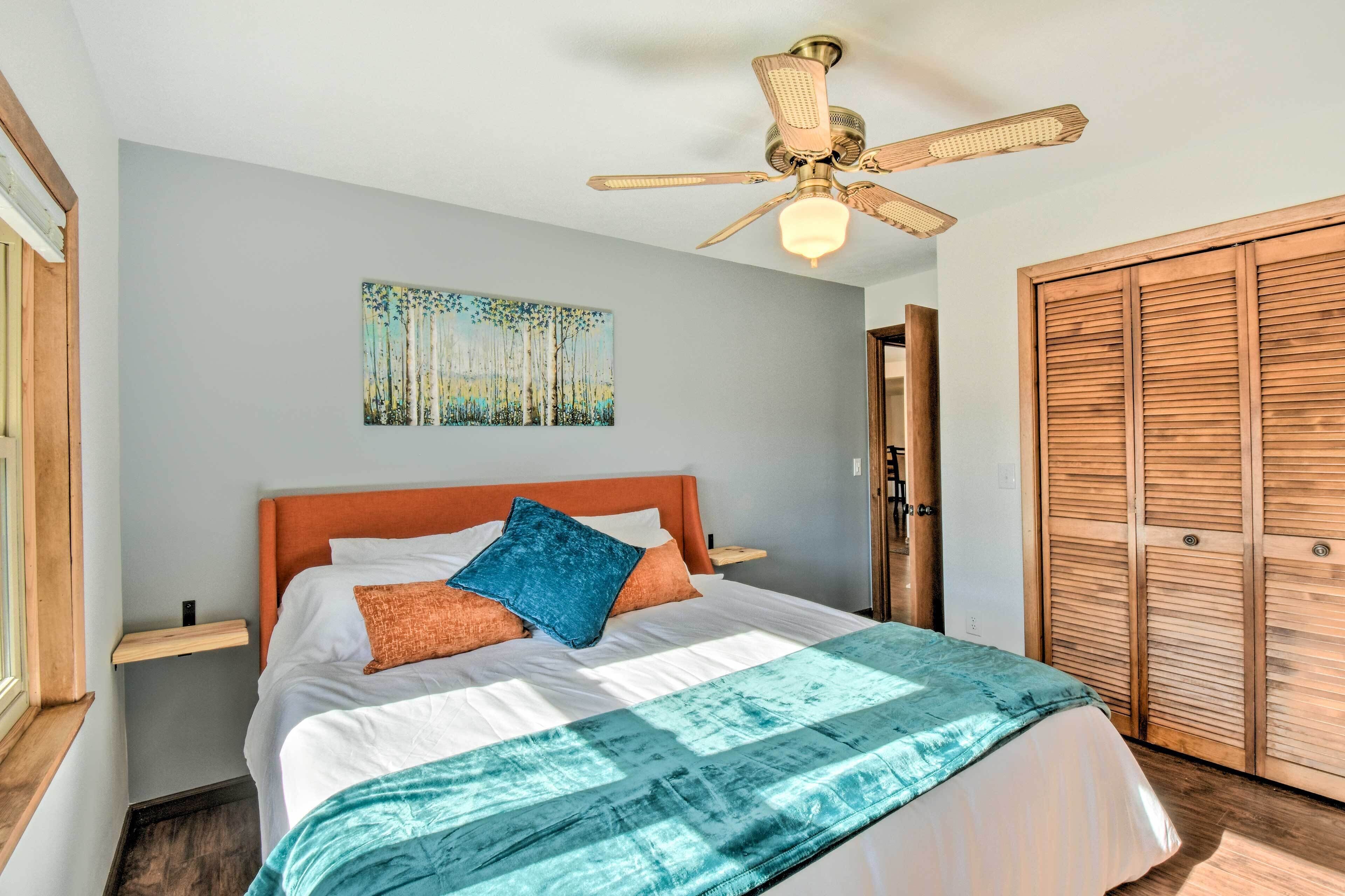 A bedroom with a bed, a ceiling fan, a wooden wardrobe, and a painting on the wall.