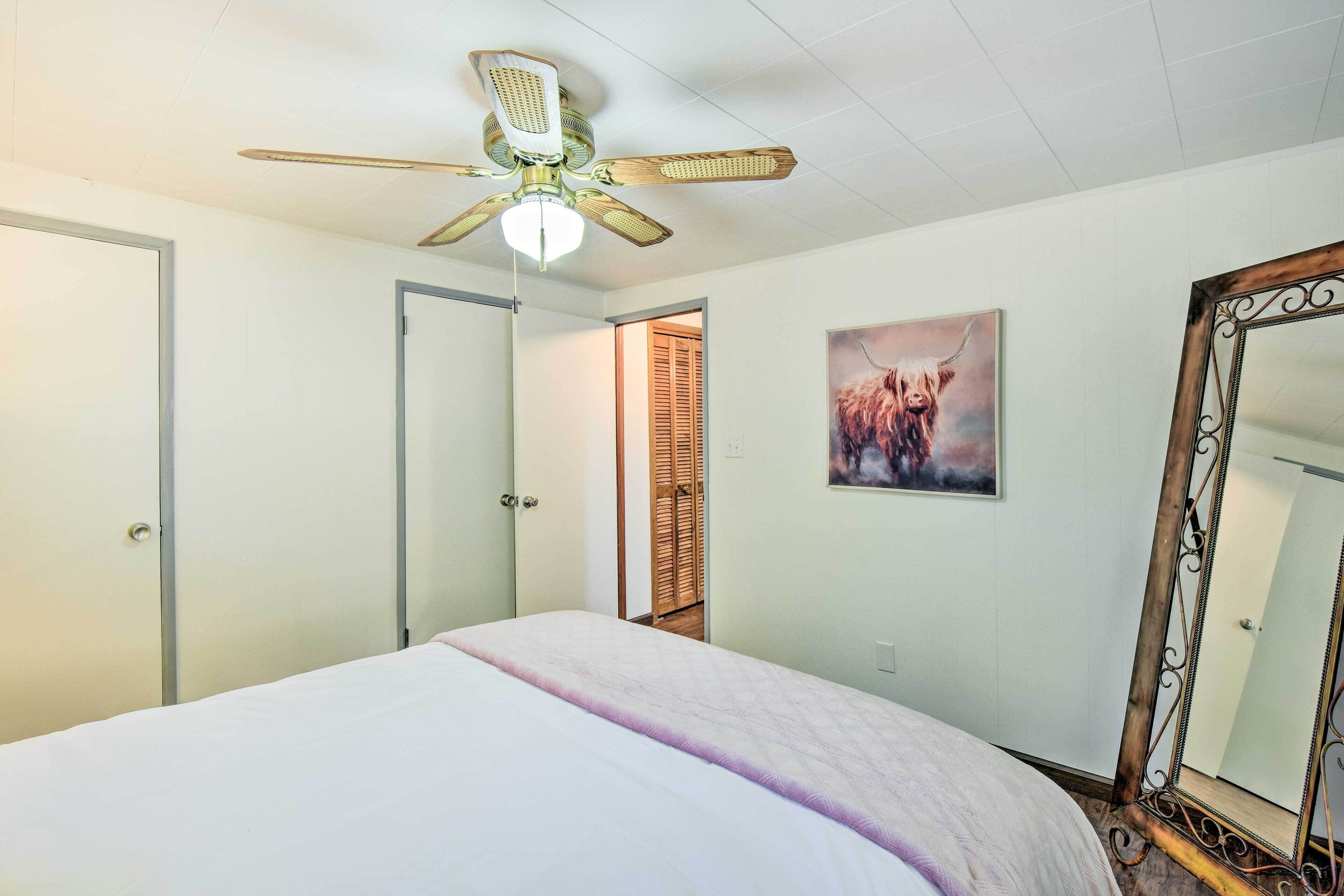 A bedroom with a bed, a ceiling fan, a door, a mirror, and a painting on the wall.
