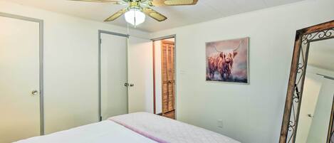 A bedroom with a bed, a ceiling fan, a door, a mirror, and a painting on the wall.