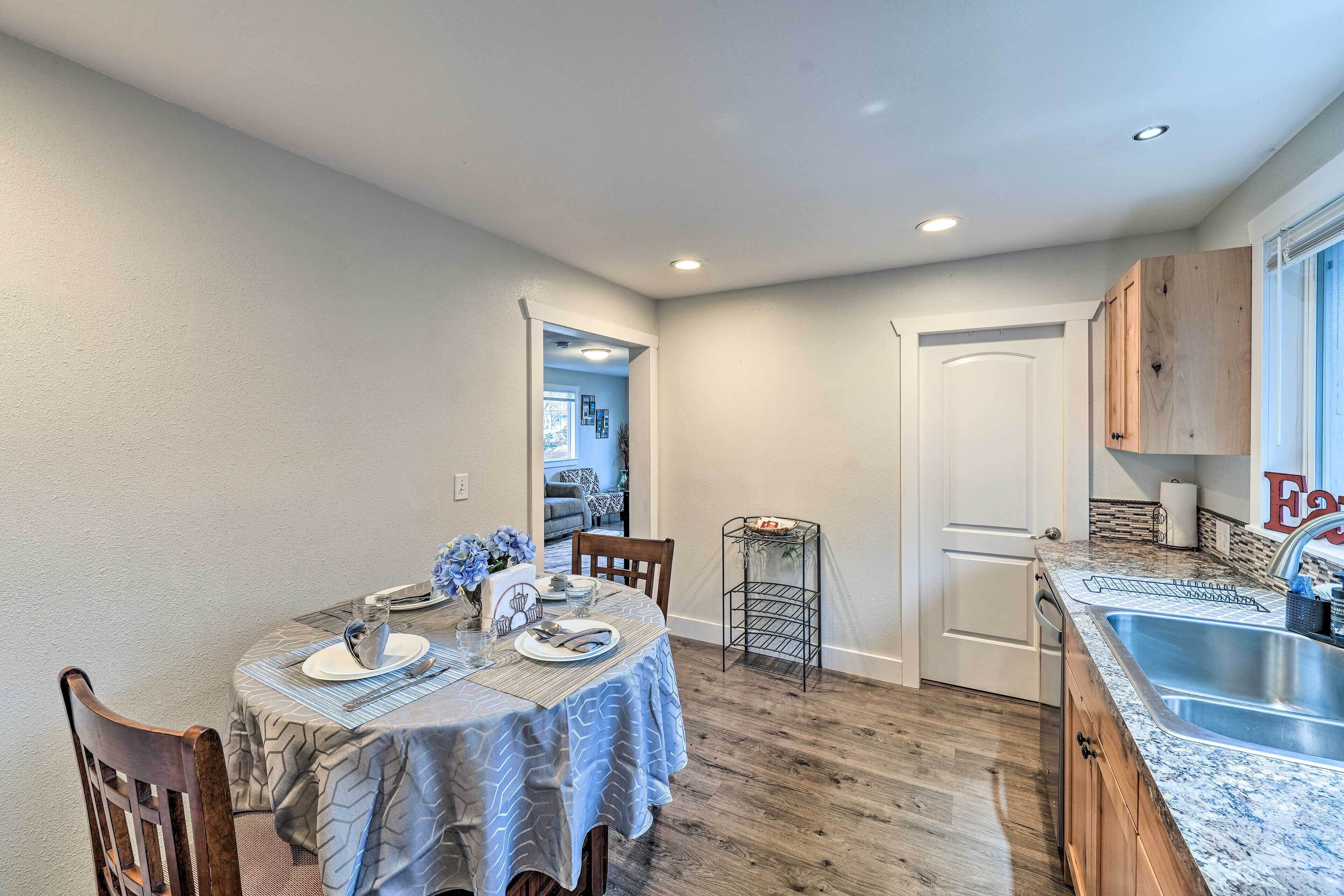 A dining area with a table set for two, a kitchen with granite countertops, and a door leading to another room.