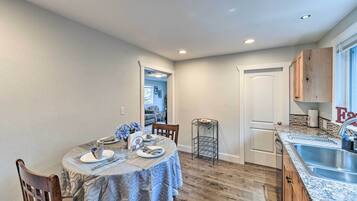 A dining area with a table set for two, a kitchen with granite countertops, and a door leading to another room.
