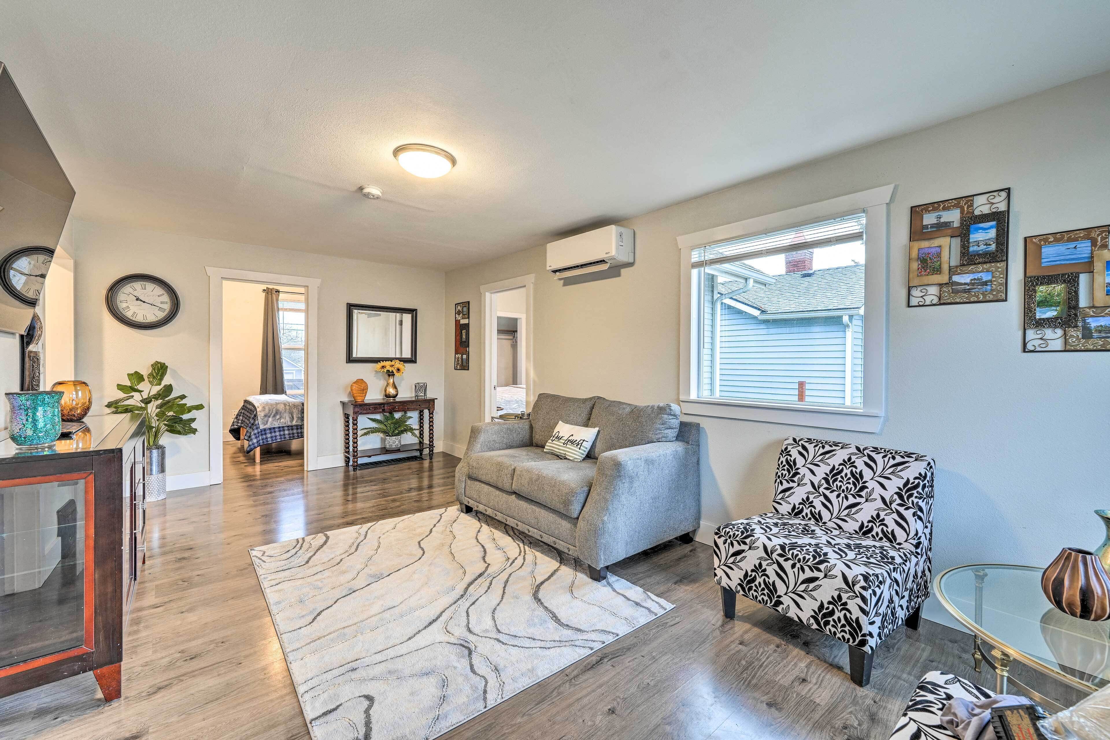 A living room with a grey sofa, a patterned armchair, a glass coffee table, and a marble rug.