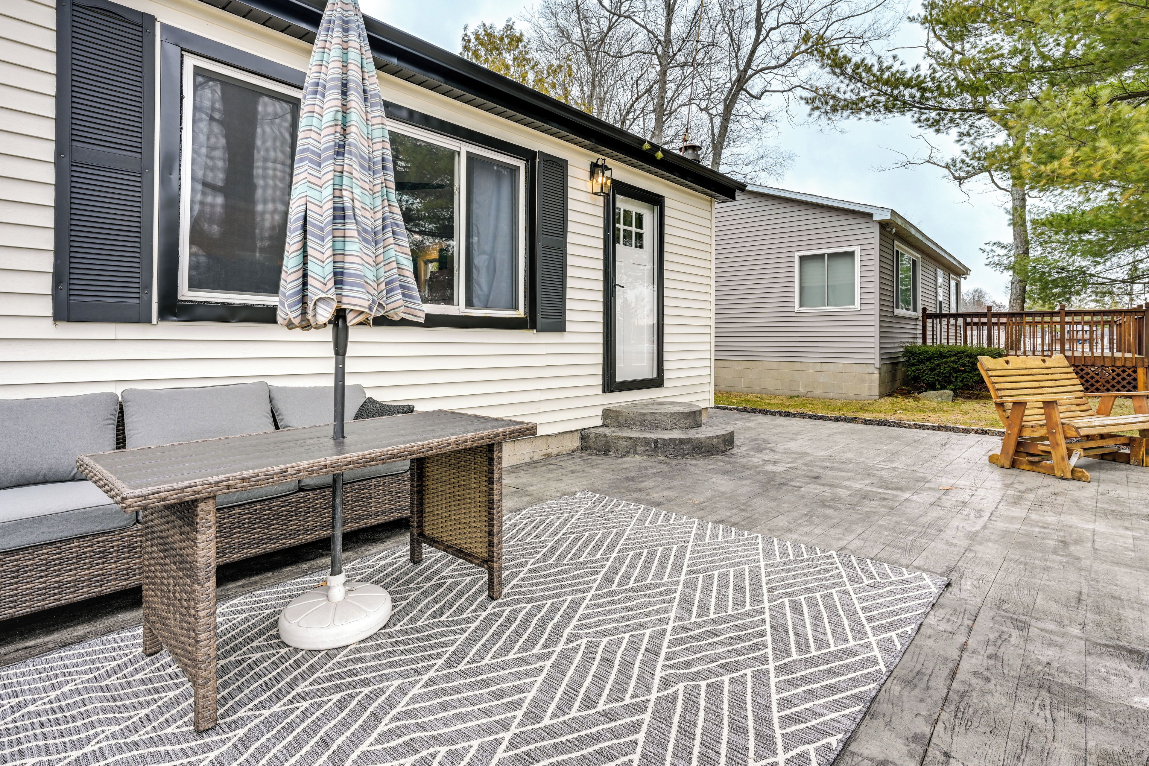 A patio area with a wicker table and chairs, a striped umbrella, and a patterned rug.