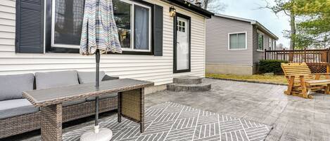 A patio area with a wicker table and chairs, a striped umbrella, and a patterned rug.